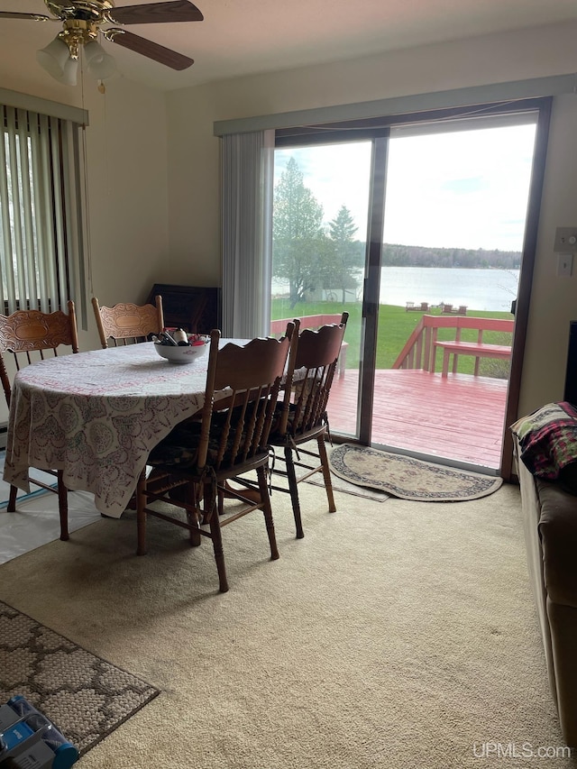 carpeted dining space with ceiling fan, a water view, and a healthy amount of sunlight