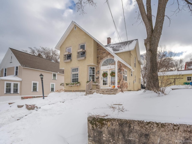 view of snowy property featuring stone siding, a chimney, and stucco siding