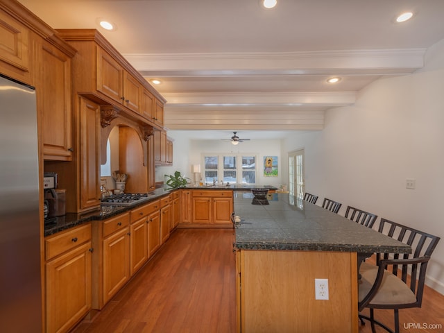 kitchen featuring light wood-style flooring, beamed ceiling, a peninsula, stainless steel appliances, and a kitchen bar