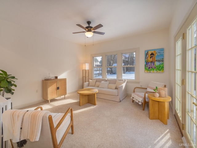 living room featuring baseboards, a ceiling fan, and light colored carpet