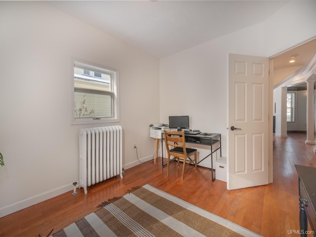 home office with radiator, decorative columns, baseboards, and wood finished floors