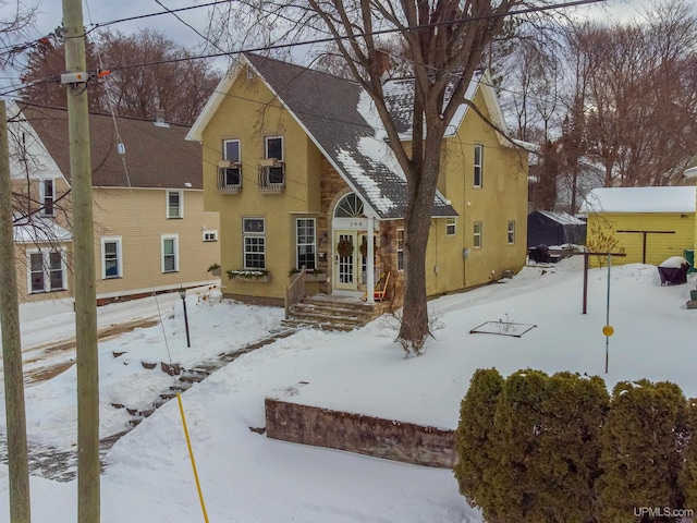 snow covered rear of property featuring a shingled roof and stucco siding