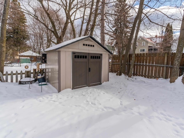 snow covered structure featuring a storage shed, an outdoor structure, and fence