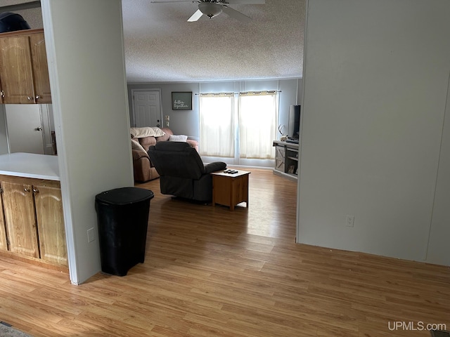 living room with ceiling fan, a textured ceiling, and light wood-type flooring