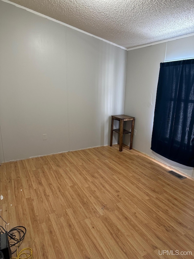 spare room featuring crown molding, wood-type flooring, and a textured ceiling