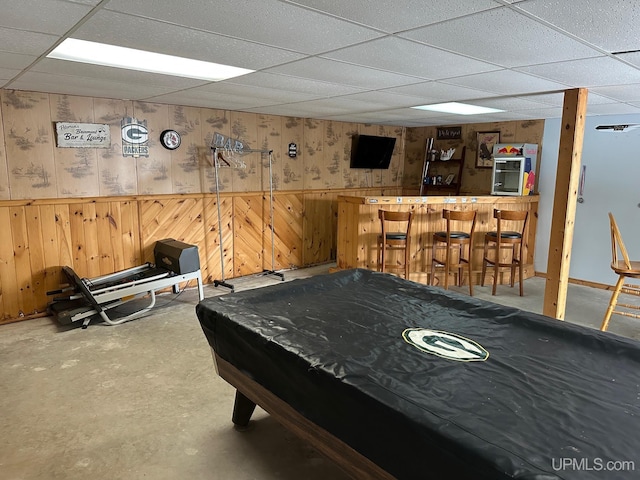 game room with bar, wooden walls, concrete floors, and a drop ceiling