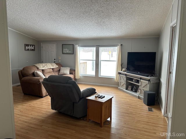 living room with ornamental molding, a textured ceiling, and light hardwood / wood-style flooring