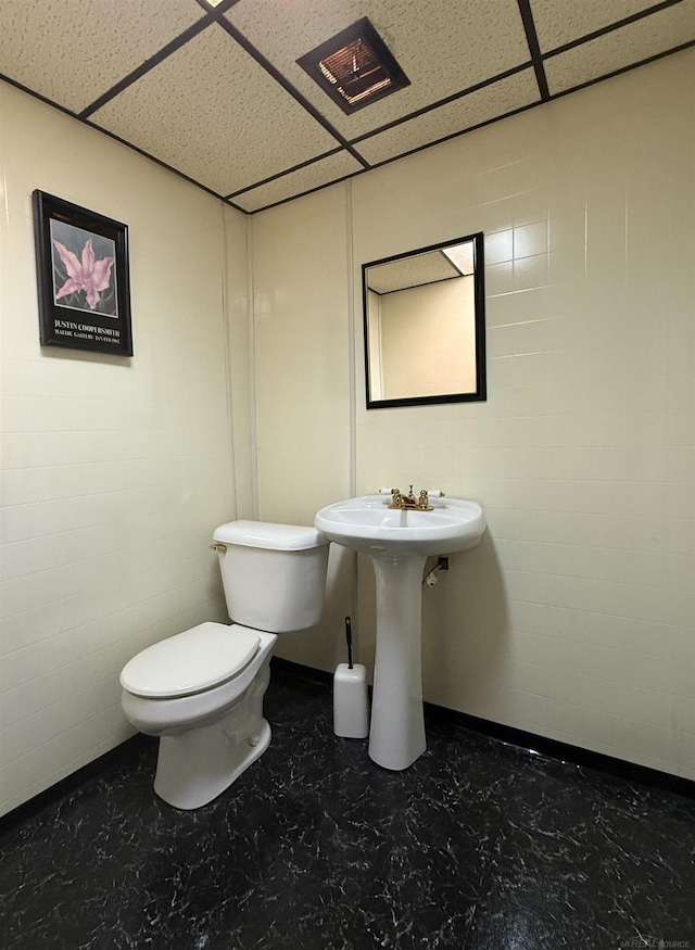 bathroom with a paneled ceiling, toilet, and sink