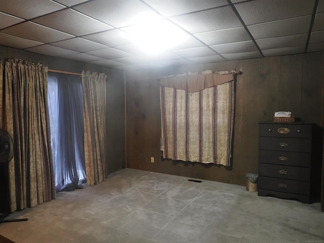 empty room featuring carpet floors, a drop ceiling, visible vents, and wooden walls