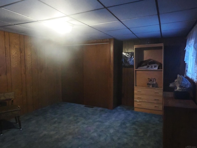 finished basement with dark colored carpet, wood walls, and a paneled ceiling