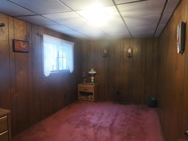 empty room featuring a paneled ceiling, wooden walls, and carpet flooring