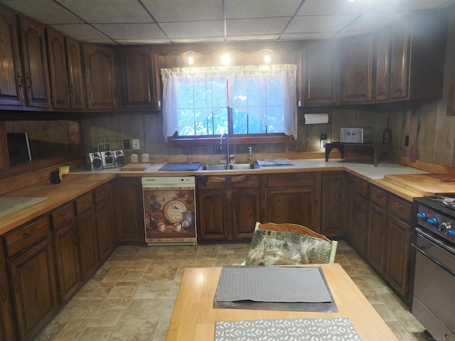 kitchen with dark brown cabinetry, a drop ceiling, dishwashing machine, stove, and a sink