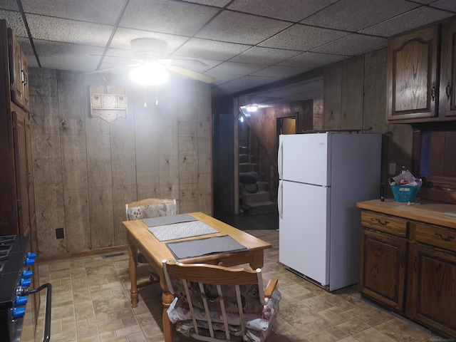 interior space with light countertops, a paneled ceiling, freestanding refrigerator, and wooden walls