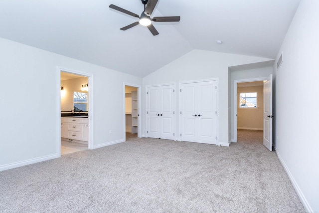 unfurnished bedroom featuring lofted ceiling, ceiling fan, connected bathroom, light carpet, and multiple closets