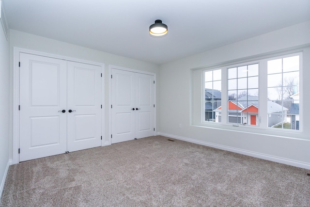 unfurnished bedroom featuring multiple closets and light colored carpet