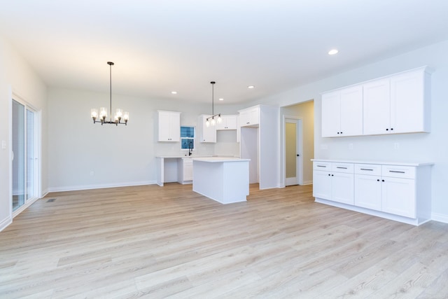 kitchen featuring a center island, a notable chandelier, white cabinets, decorative light fixtures, and light wood-type flooring