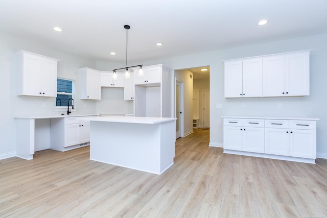 kitchen featuring hanging light fixtures, white cabinetry, a kitchen island, and light hardwood / wood-style floors