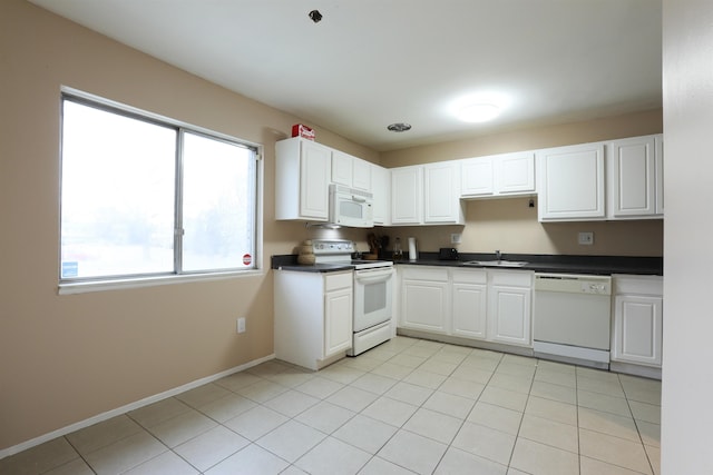 kitchen with white appliances, baseboards, white cabinets, dark countertops, and a sink