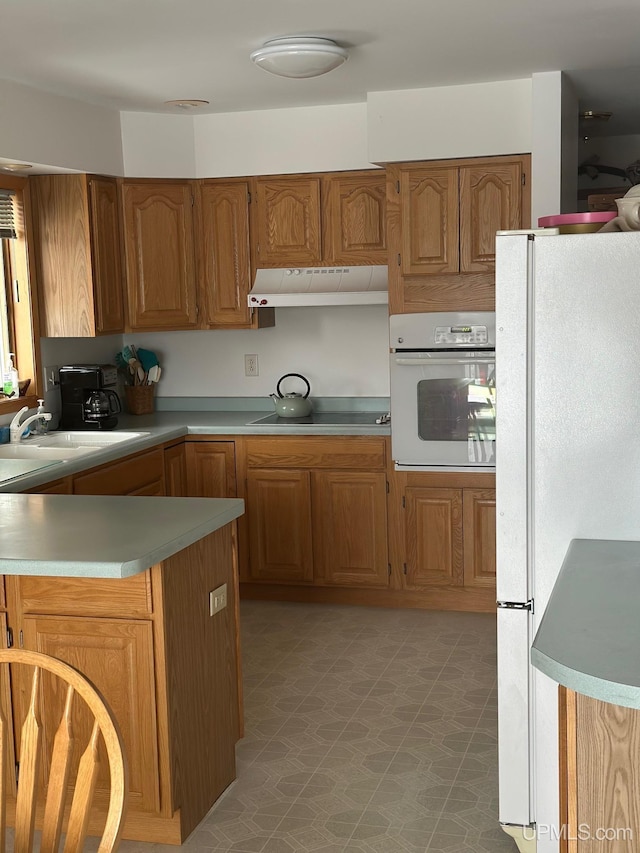 kitchen with brown cabinets, light countertops, a sink, white appliances, and under cabinet range hood