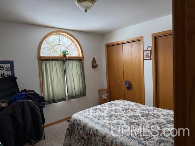 bedroom with carpet floors, baseboards, and two closets