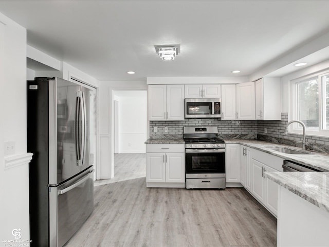 kitchen with stainless steel appliances, white cabinetry, light stone countertops, and sink