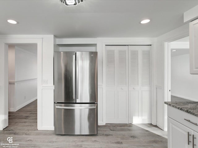 kitchen featuring white cabinetry, light hardwood / wood-style flooring, stainless steel fridge, and dark stone counters