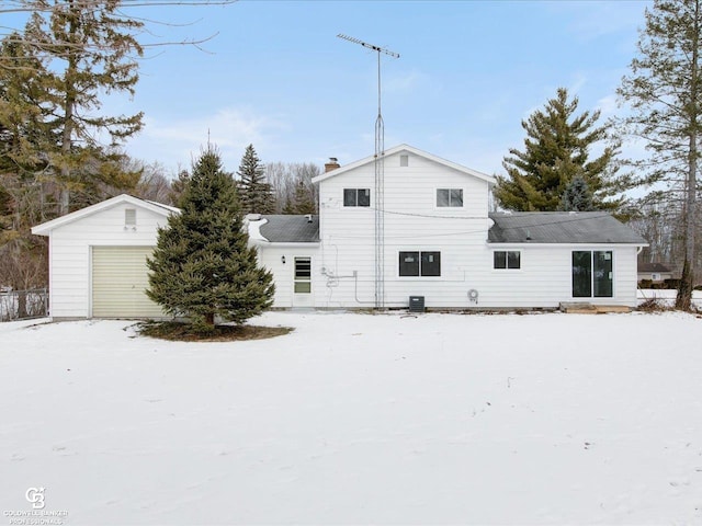 snow covered back of property with a garage and central AC