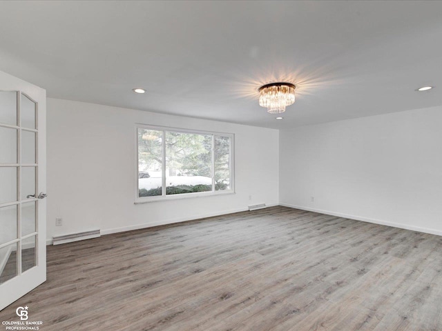 empty room with a baseboard heating unit, a notable chandelier, and light wood-type flooring