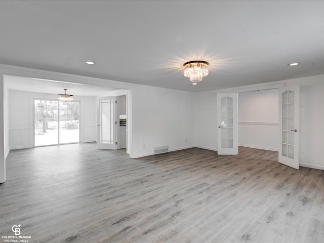 spare room featuring french doors, light hardwood / wood-style floors, and an inviting chandelier