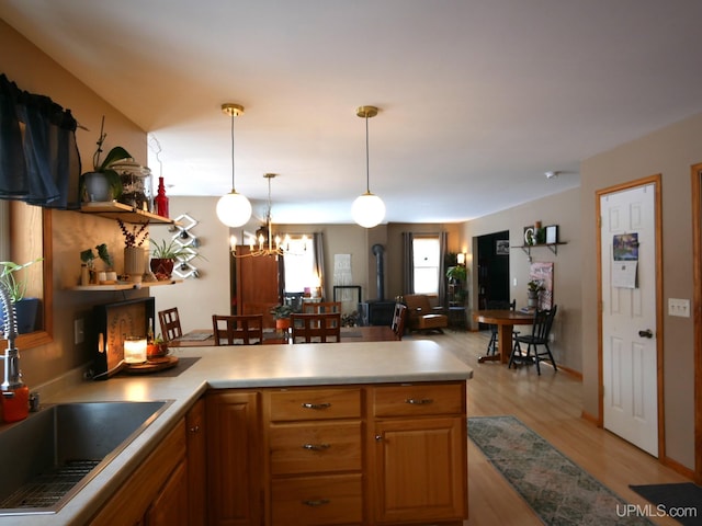 kitchen with sink, hanging light fixtures, light wood-type flooring, a chandelier, and a wood stove