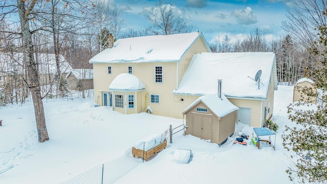 snow covered rear of property featuring a storage unit