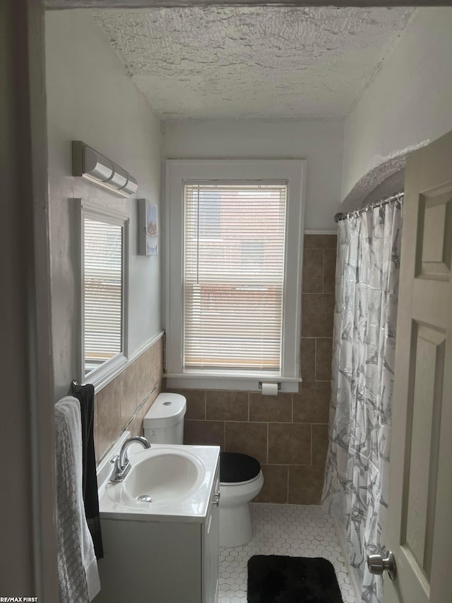 bathroom featuring tile walls, vanity, walk in shower, toilet, and a textured ceiling