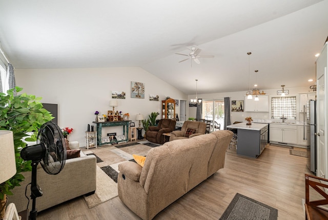 living room with ceiling fan with notable chandelier, sink, vaulted ceiling, and light wood-type flooring