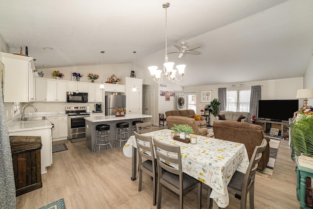 dining space with sink, ceiling fan with notable chandelier, vaulted ceiling, and light wood-type flooring