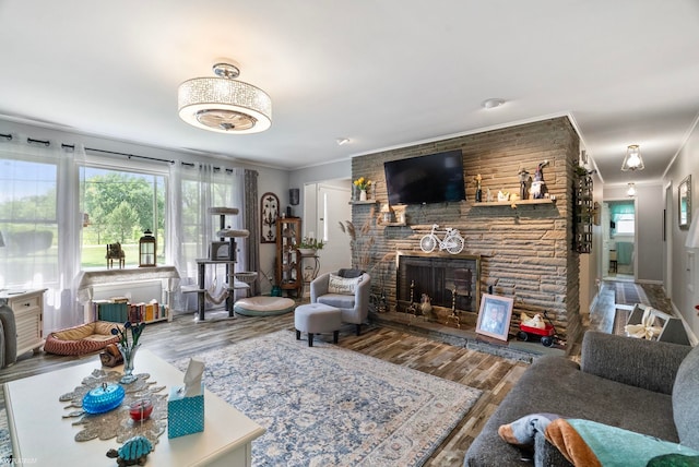 living room with hardwood / wood-style flooring, ornamental molding, and a stone fireplace