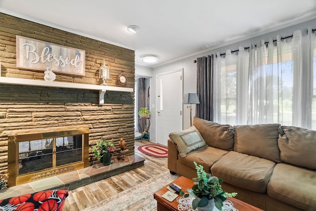 living room with crown molding, a stone fireplace, and hardwood / wood-style flooring