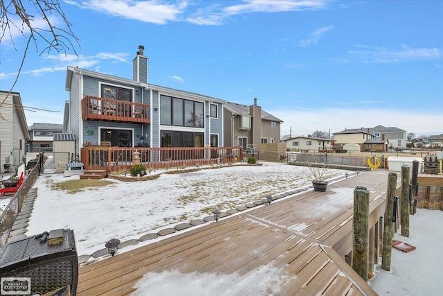 snow covered back of property with a balcony, fence, a residential view, and a chimney