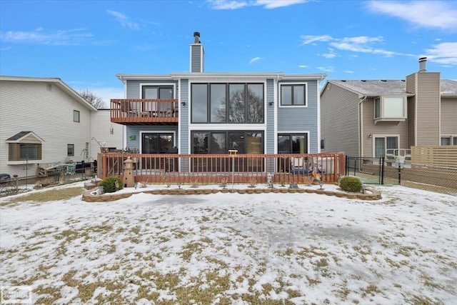 snow covered back of property with a wooden deck, a balcony, fence, and a chimney