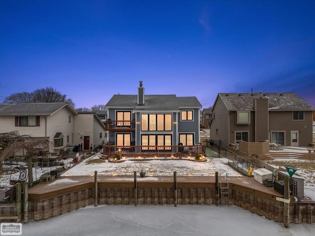 snow covered house featuring a balcony, a fenced front yard, and a chimney