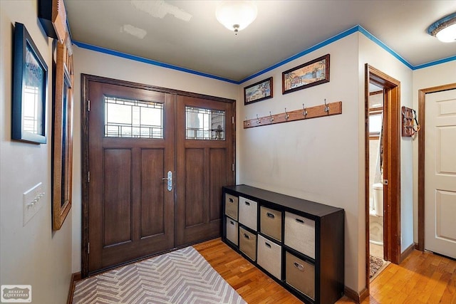 foyer entrance featuring crown molding, light wood-style flooring, and baseboards