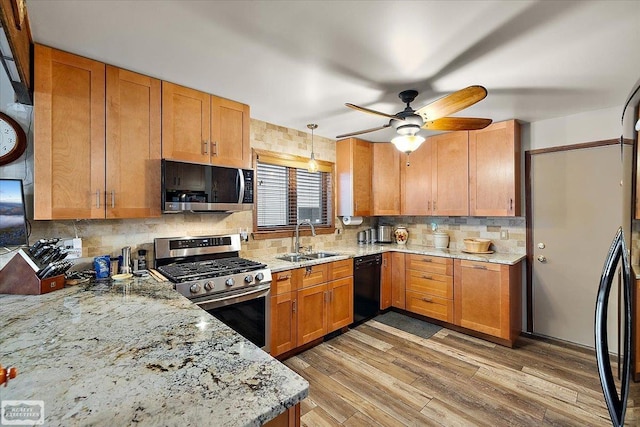 kitchen featuring light wood-style flooring, a sink, backsplash, stainless steel appliances, and light stone countertops