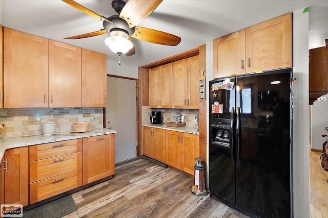 kitchen with a ceiling fan, black fridge, light stone counters, tasteful backsplash, and wood finished floors