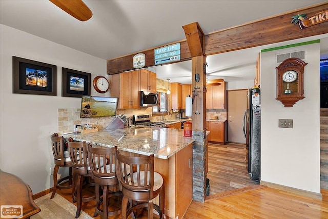 kitchen with a peninsula, light wood-style flooring, a sink, appliances with stainless steel finishes, and backsplash