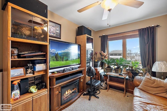 living area with a glass covered fireplace and a ceiling fan