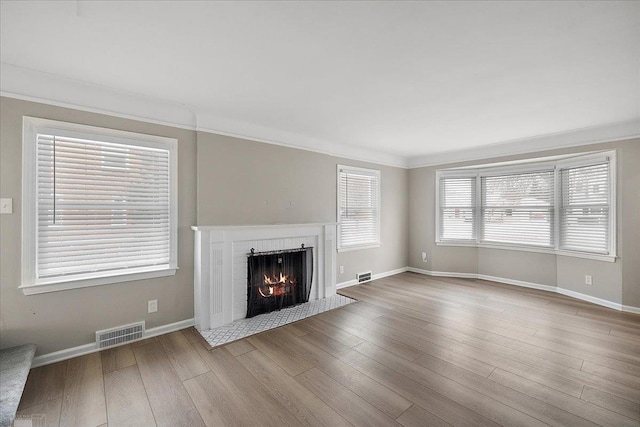 unfurnished living room featuring wood-type flooring, ornamental molding, and a fireplace