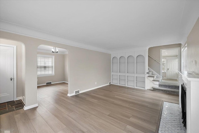 unfurnished living room featuring built in features, ornamental molding, and light wood-type flooring