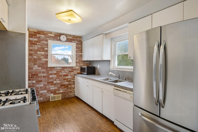 kitchen featuring white cabinetry, brick wall, stainless steel appliances, and sink