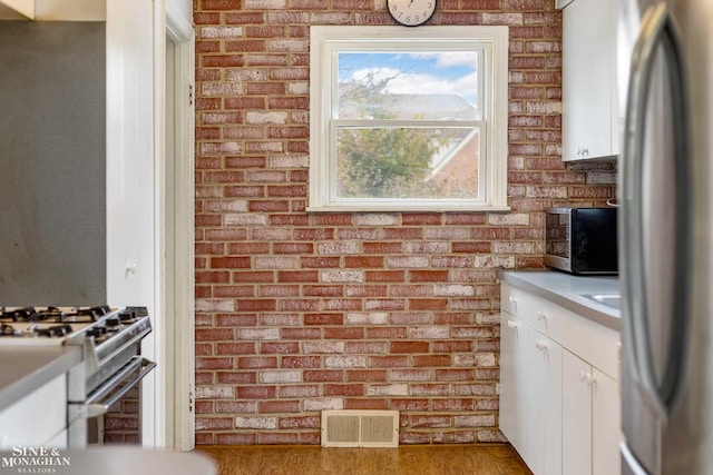 kitchen with stainless steel appliances, white cabinetry, brick wall, and hardwood / wood-style flooring