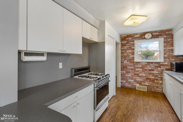 kitchen with white cabinets, wood-type flooring, white gas stove, and brick wall