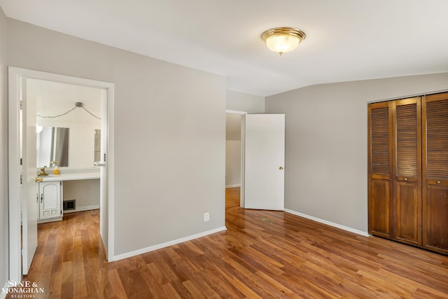 unfurnished bedroom with vaulted ceiling, a closet, and light wood-type flooring